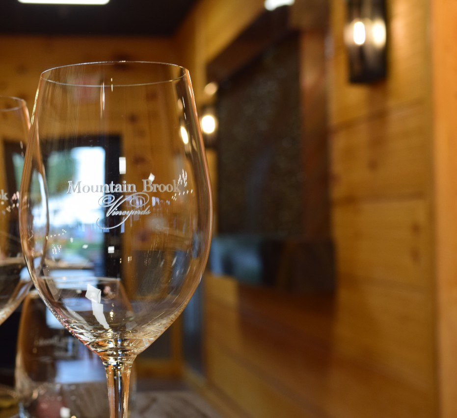 Empty wine glass with Mountain Brook Vineyards logo, in a warmly lit wooden interior.